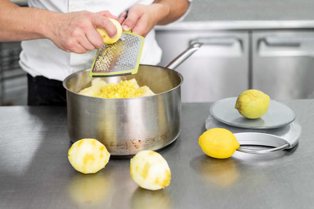 A Pastry chef&rsquo;s hand grates lemon in commercial kitchen. Chef grates limes on the grater to get zest for cooking, making of pastry, healthy food, natural supplements close-up. High quality photo. A Pastry chef&rsquo;s hand grates lemon in commercial kitchen. Chef grates limes on the grater to get zest for cooking, making of pastry, healthy food, natural supplements close-up.