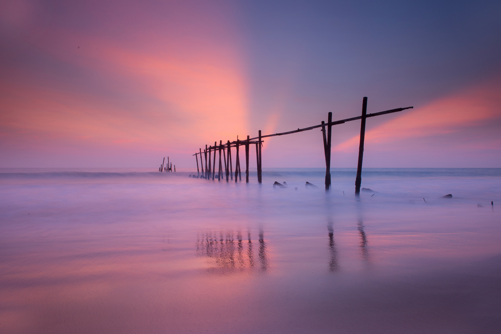 Beautiful old Wooden Bridge, wooden fisherman bridge. Beautiful of seascape Reflections from the sun at the sand, sunset at the sea southern of Thailand  wooden bridge in pilai beach Phang Nga Thailand at Pilai beach, Phang Nga, Thailand.