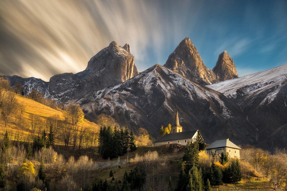 Church in a village in the french alps with mountains 3000 meters high. first autumn snowfall with brown . Moving clouds and long exposure