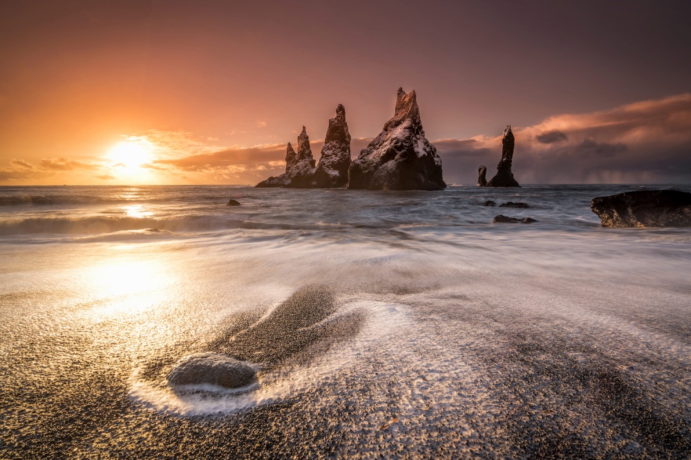 Beach in Iceland with black sand and rock formations at the background at twilight