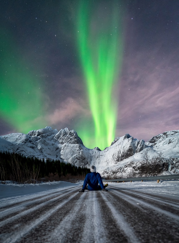 Man sitting on a snowy road looking at northern lights