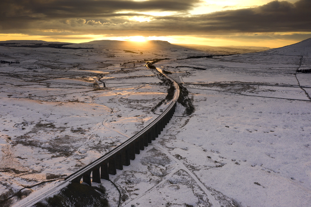 Winter Ariel picture of Yorkshire landmark Ribblehead Viaduct, North Yorkshire, The Ribblehead Viaduct or Batty Moss Viaduct carries the Settle-Carlisle railway across Batty Moss in the Ribble Valley at Ribblehead, in North Yorkshire, England. The viaduct, built by the Midland Railway, is 28 miles (45 km) north-west of Skipton and 26 miles (42 km) south-east of Kendal. It is a Grade II* listed structure.[1] Ribblehead Viaduct is the longest and the third tallest structure on the Settle-Carlisle line.The viaduct was designed by John Sydney Crossley, chief engineer of the Midland Railway, who was responsible for the design and construction of all major structures along the line. The viaduct was necessitated by the challenging terrain of the route. Construction began in late 1869. It necessitated a large workforce, up to 2,300 men, most of whom lived in shanty towns set up near its base. Over 100 men lost their lives during its construction. The Settle to Carlisle line was the last main railway in Britain to be constructed primarily with manual labour.