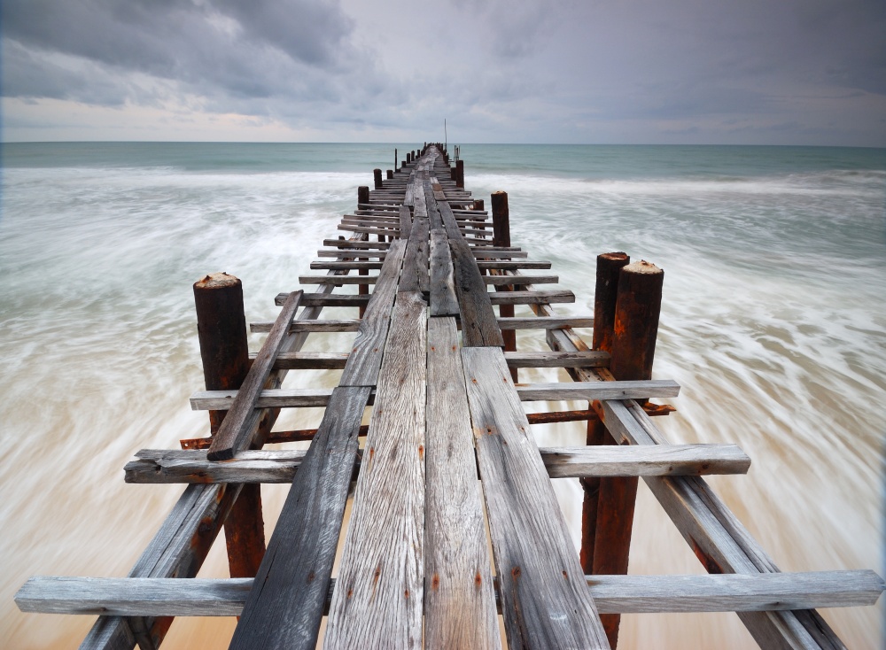 Filed wooden bridge into the sea after sunset on the beach