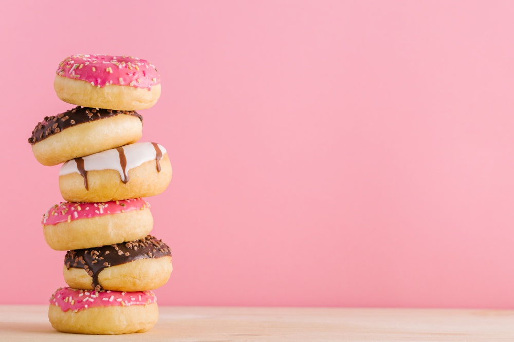 Stack of tasty sweet different colored donuts on a table on pink background.. Stack of different donuts on pink