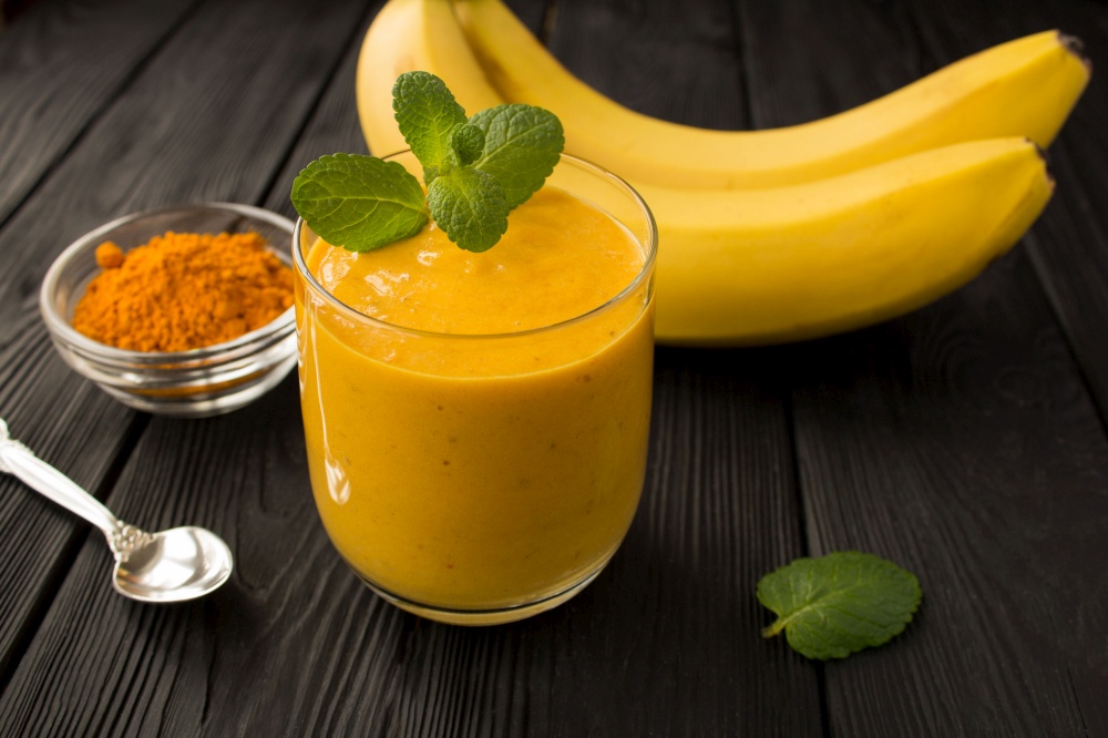 Smoothies with banana and turmeric on the black wooden background