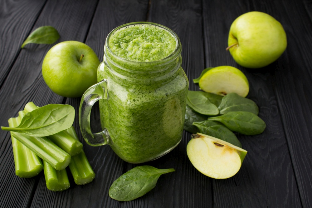 Green smoothies with spinach, apple and celery  on the black wooden background