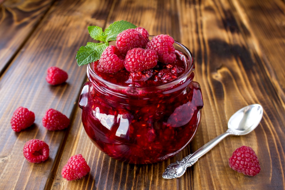 Raspberry  jam in the glass jar on the  brown wooden  background. Closeup.