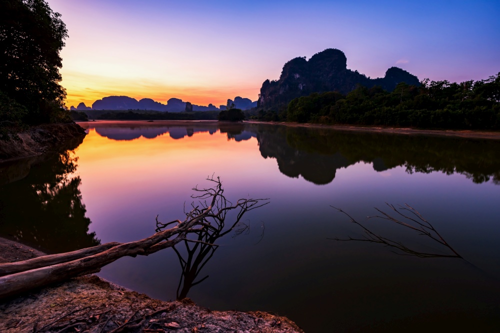 Natural swamp or beautiful reservoir and Limestone mountains at dawn with twilight sky, Nong Thale, Krabi, Thailand. travel destination after covid-19 lock down. Focus at tree trunk.