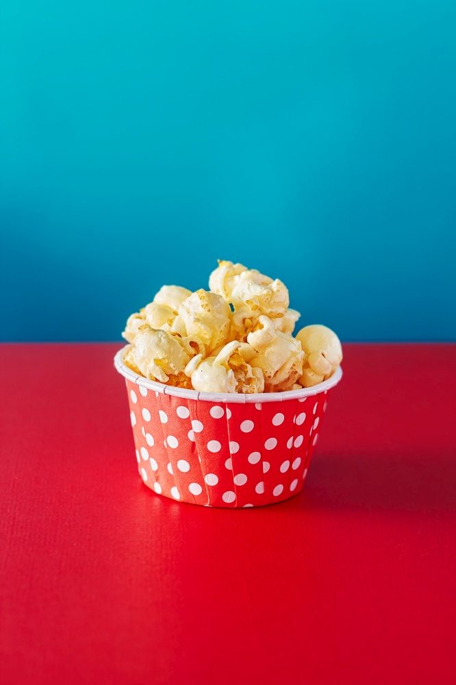 A red paper cup with popcorn against orange background with spot lighting,shallow Depth of Field,Focus on popcorn.. A red paper cup with popcorn.