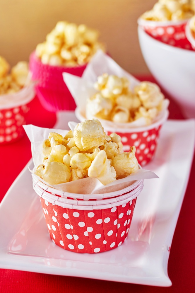 A red paper cup with popcorn against orange background with spot lighting,shallow Depth of Field,Focus on popcorn.. A red paper cup with popcorn.
