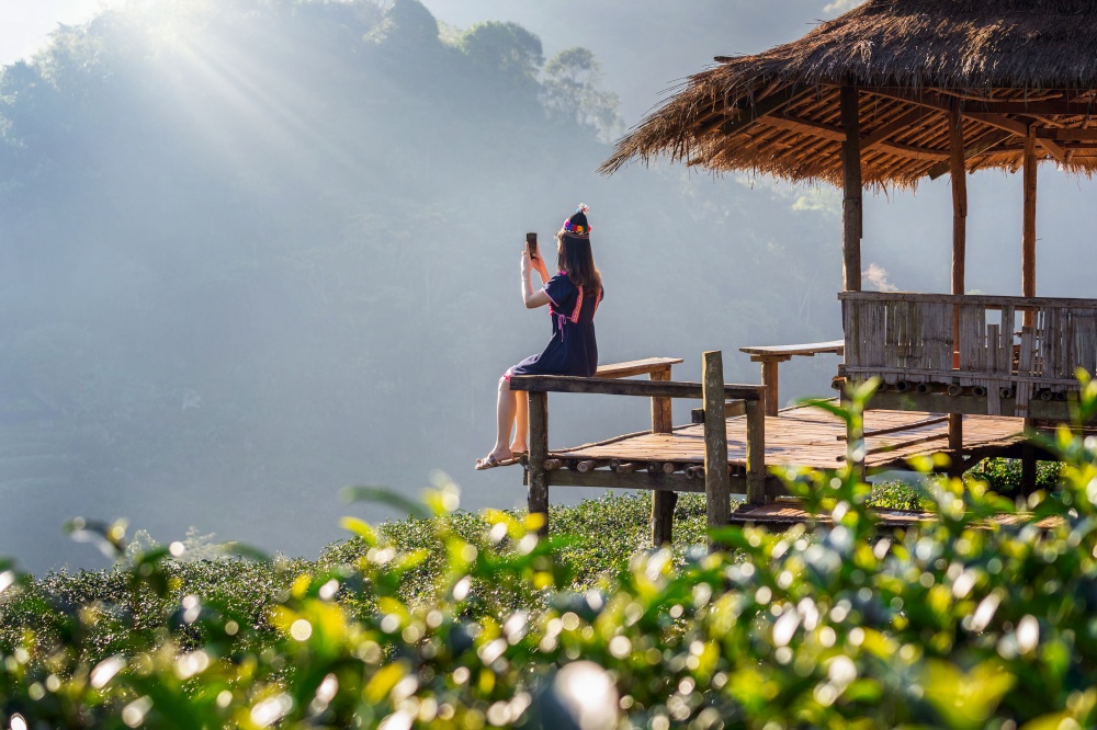 Woman wearing hill tribe dress sitting on the hut in green tea field.