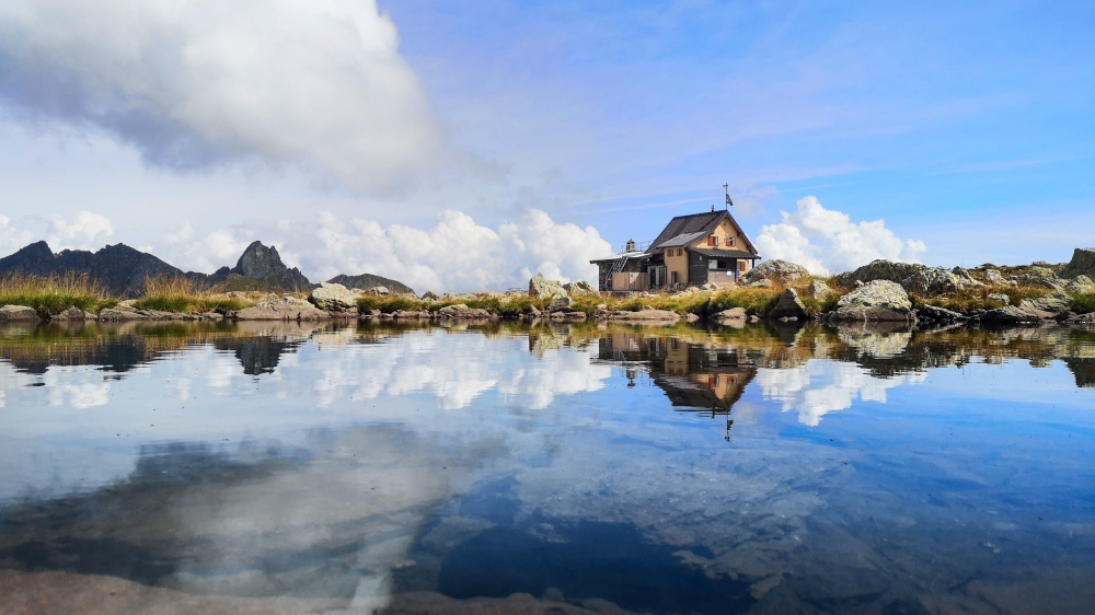 Alpine hut is reflected in a small mountain lake