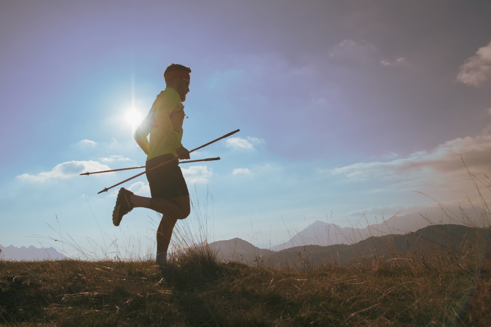 Man runs in the mountains with sticks in his hand.