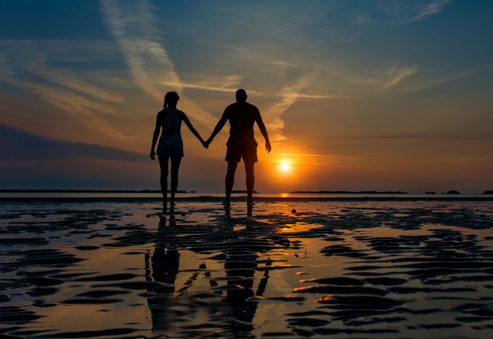 Couple hand in hand towards the sea in a dawn late summer in silhouettes