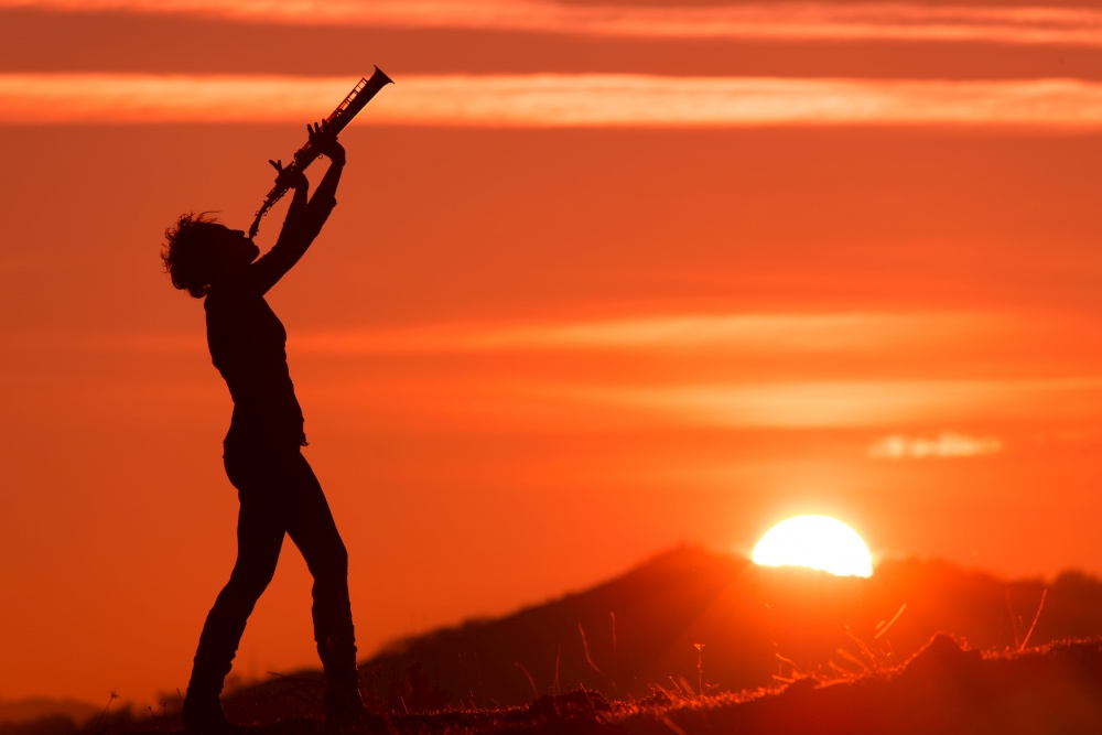 Saxophonist in silhouette sounds to the great sun setting