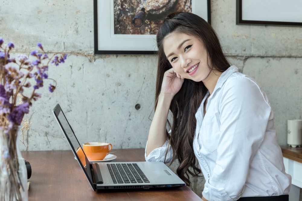 Beautiful Asian woman working with laptop and drinking coffee