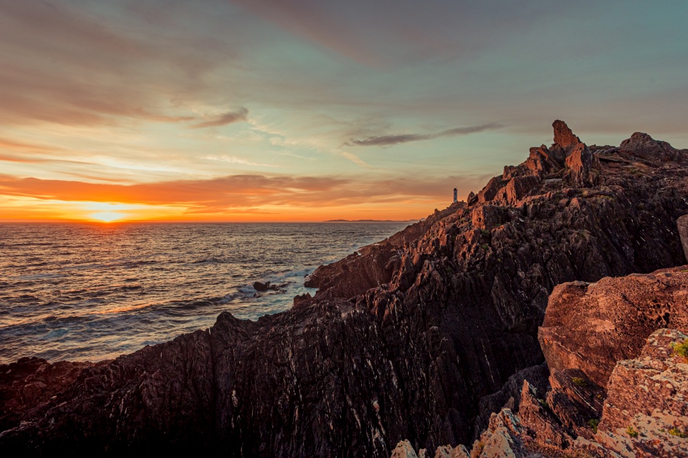 Dramatic horizontal shot of a white lighthouse during the sunset from the rocks of the coast