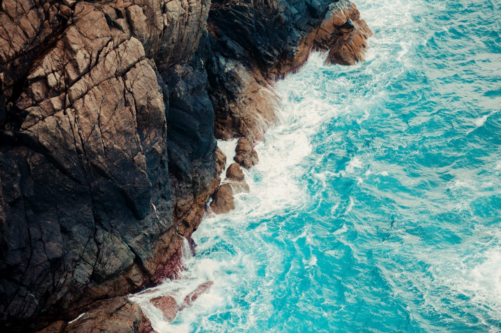 An aerial shot of the crystal water sea touching the rocks of the bottom of a mountain