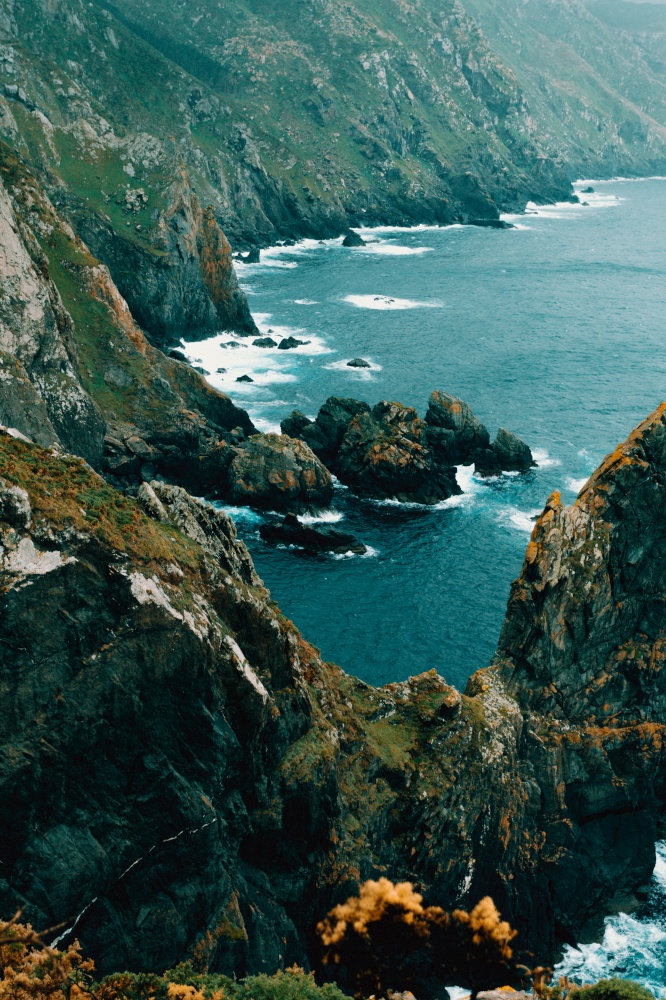 Some giant cliffs in europe with green grass and the ocean crashing against them