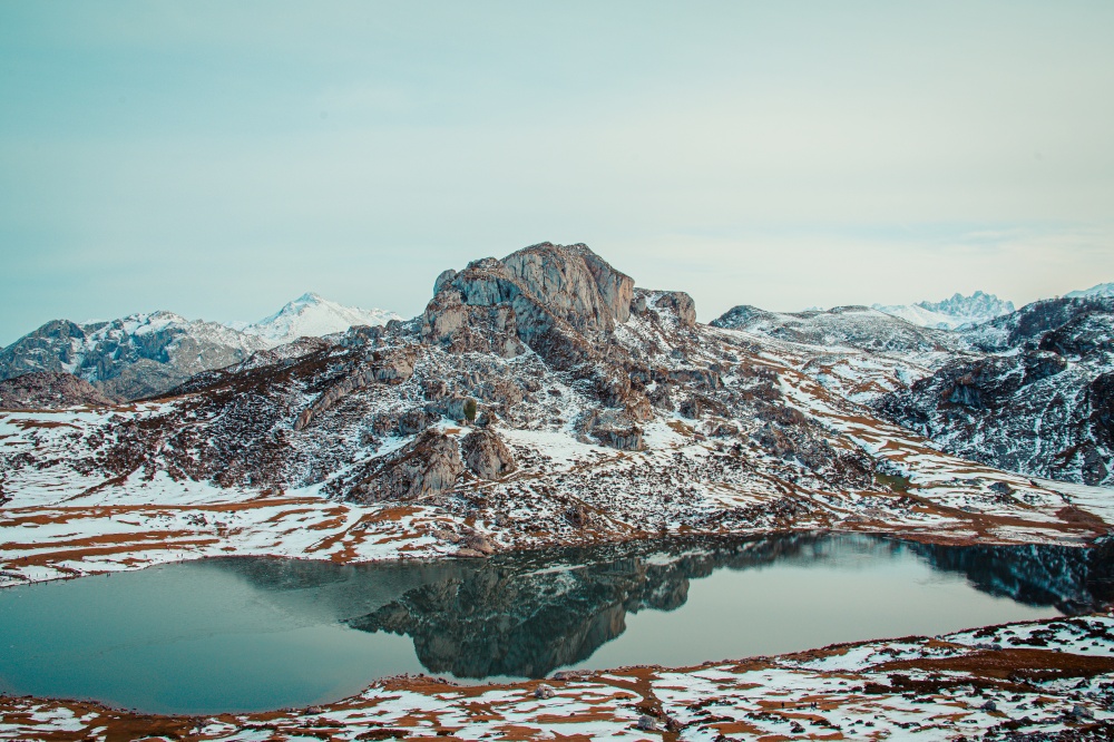 A massive rocky mountain in front of a frozen lake in the mountains of asturias