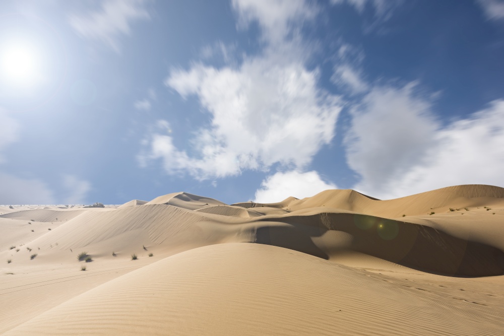 Red sand dunes with moving clouds against a blue sky with copy space