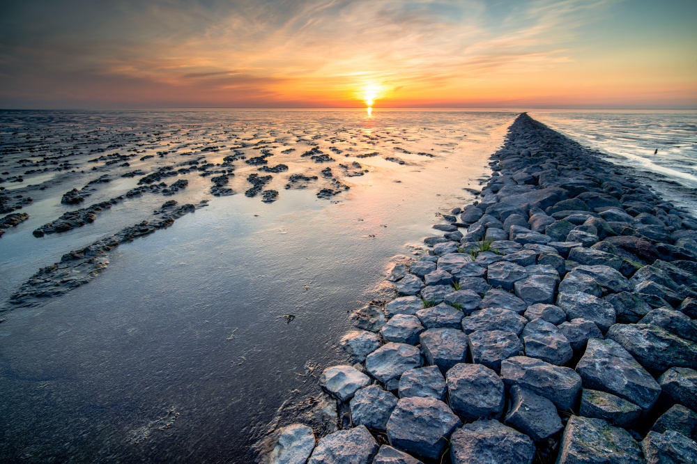Mud flat of the &rsquo;waddenzee&rsquo; during low tide under scenic dramatic sunset sky with clouds. Wadden coast twilight with mud plains
