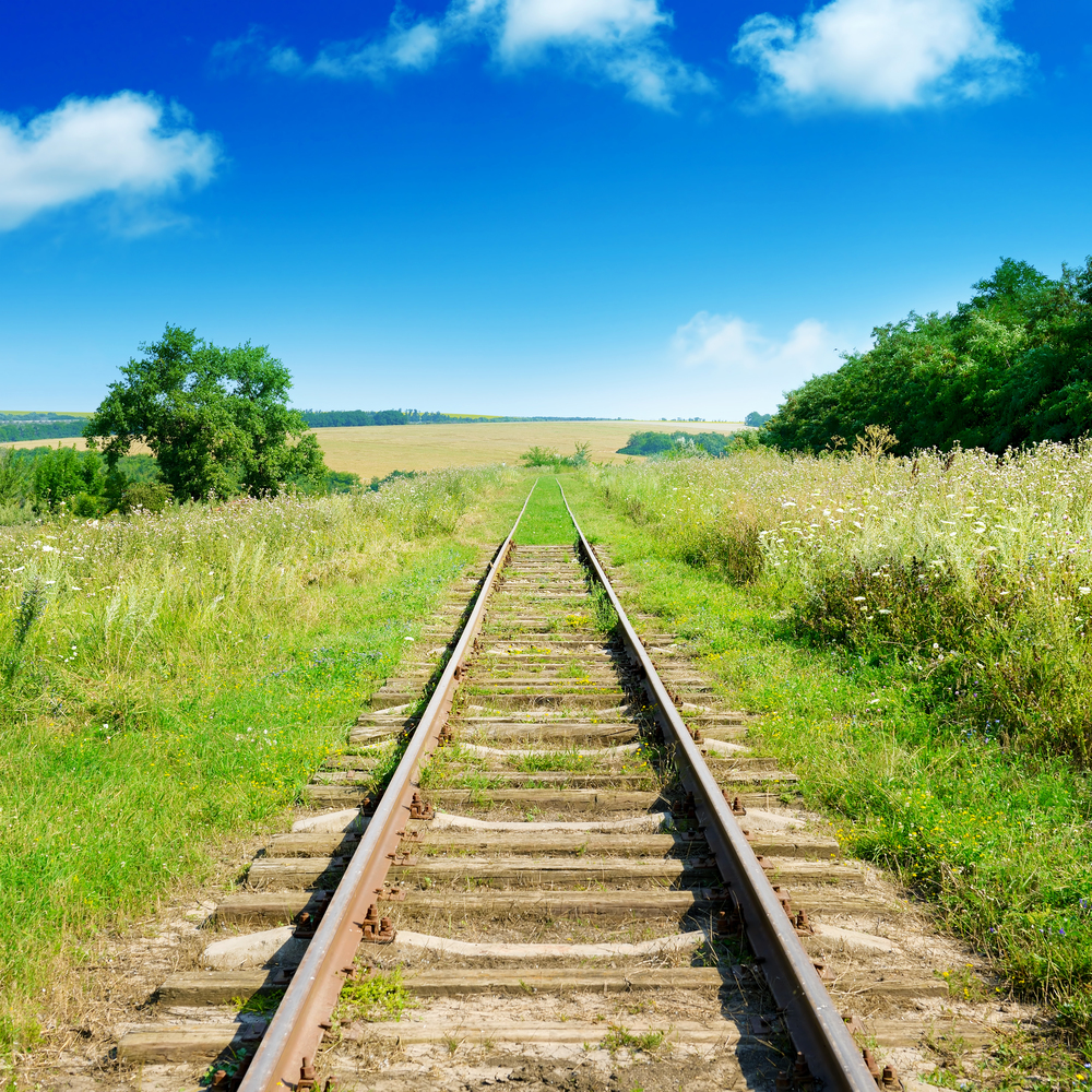Old railway track among summer fields and blue sky