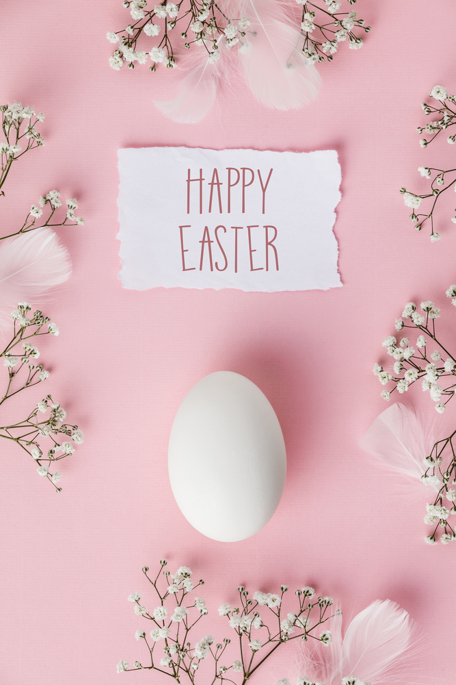 White Easter egg and flowers on pastel pink background. Happy Easter concept. Space for text