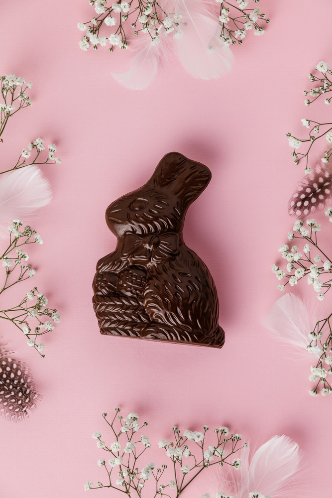 Chocolate Easter Bunny, feathers and flowers on pastel pink background. Happy Easter concept. Space for text
