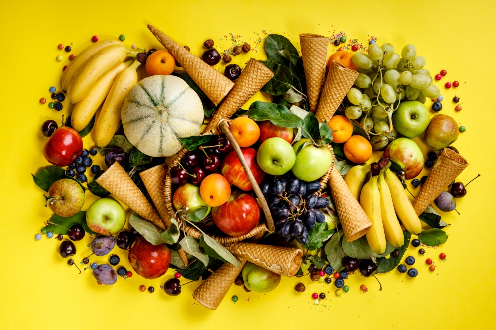 Flat-lay of fruits and berries and ice cream cones on yellow background. Top view.