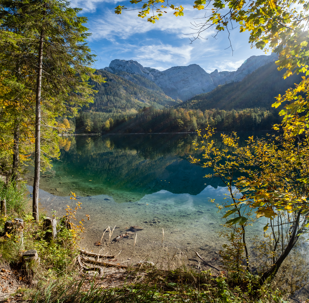 Sunny idyllic colorful autumn alpine view. Peaceful mountain lake with clear transparent water and reflections. Langbathseen lake, Upper Austria. There is some sun and lens flares effect.