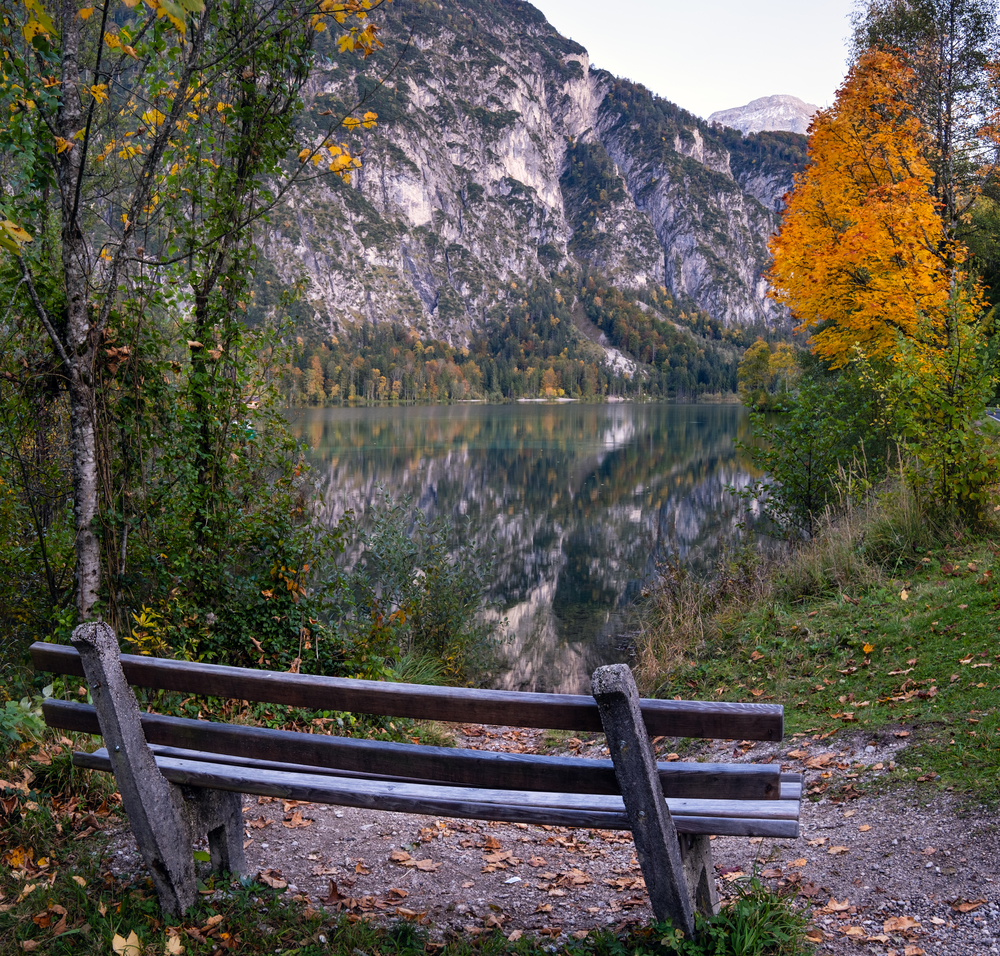 Autumn evening alpine view. Bench near peaceful mountain lake with clear transparent water and reflections.  Almsee lake, Upper Austria.