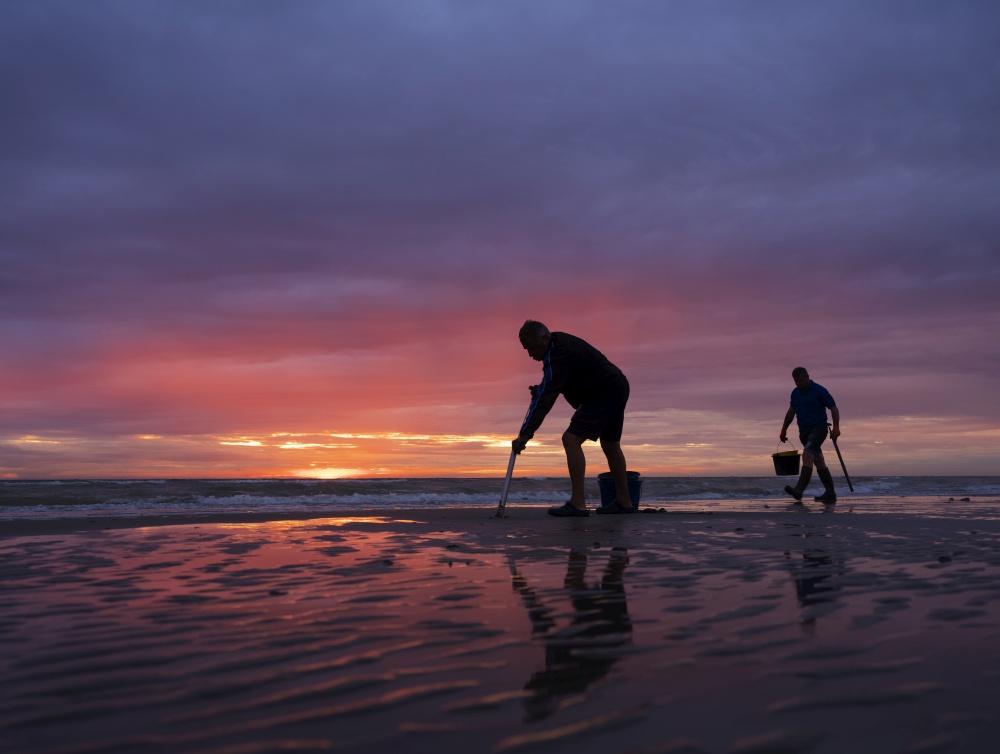 men on normandy beach during colorful sunset look for worms to use as bait for fishing