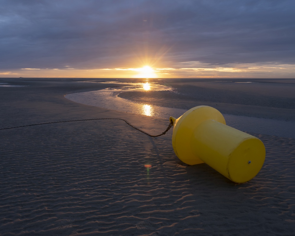 large yellow buoy on beach of normandy at sunset