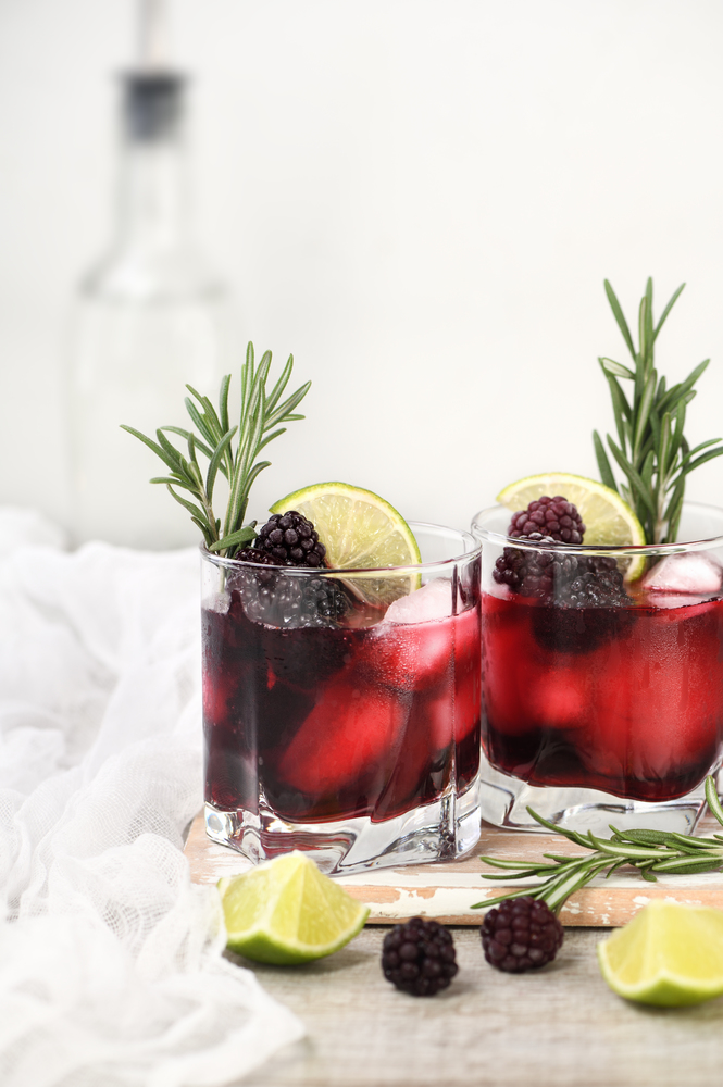 Alcoholic cocktail. Cold alcohol drink with ice, lime, blackberry and gin, decorated of rosemary.
