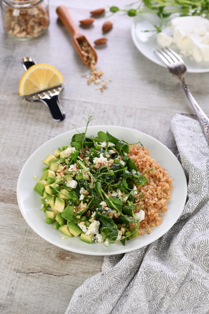 Gluten-free green vegetarian salad made of microgreen sprouts peas, avocado, quinoa, spinach, seasoned  crushed almonds with slices of feta cheese