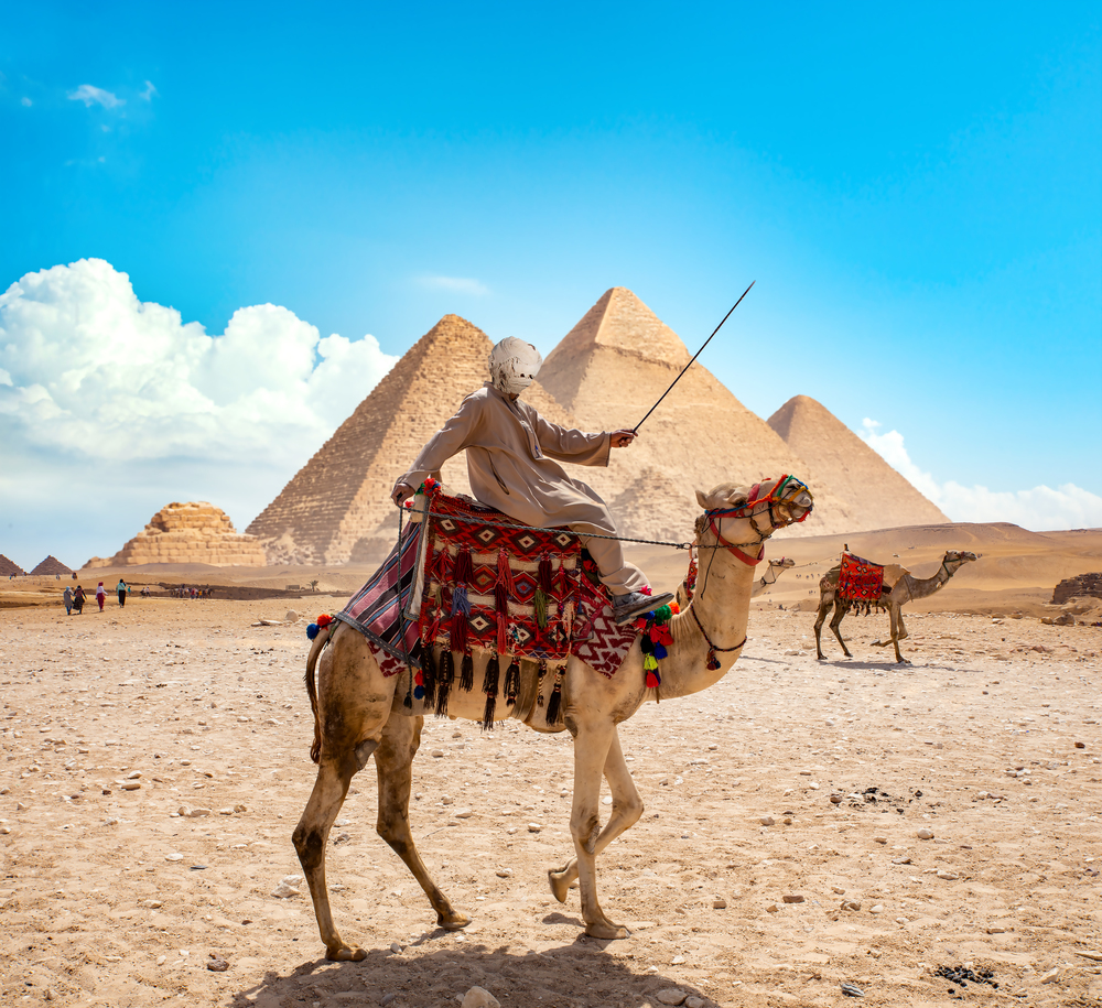 Bedouin on camel near pyramids in desert
