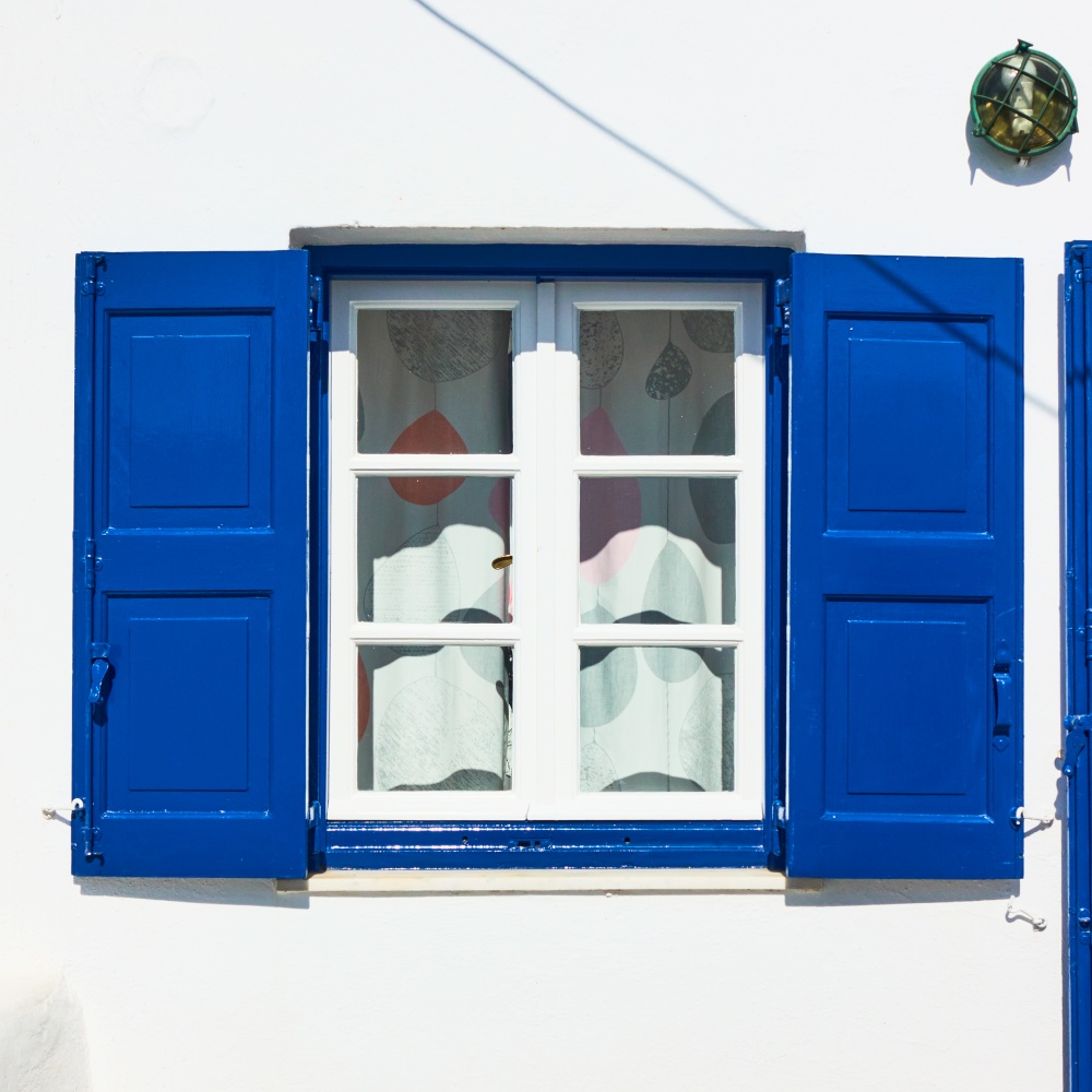 Window of a greek whitewashed house with trditional blue shutters in Mykonos island, Greece
